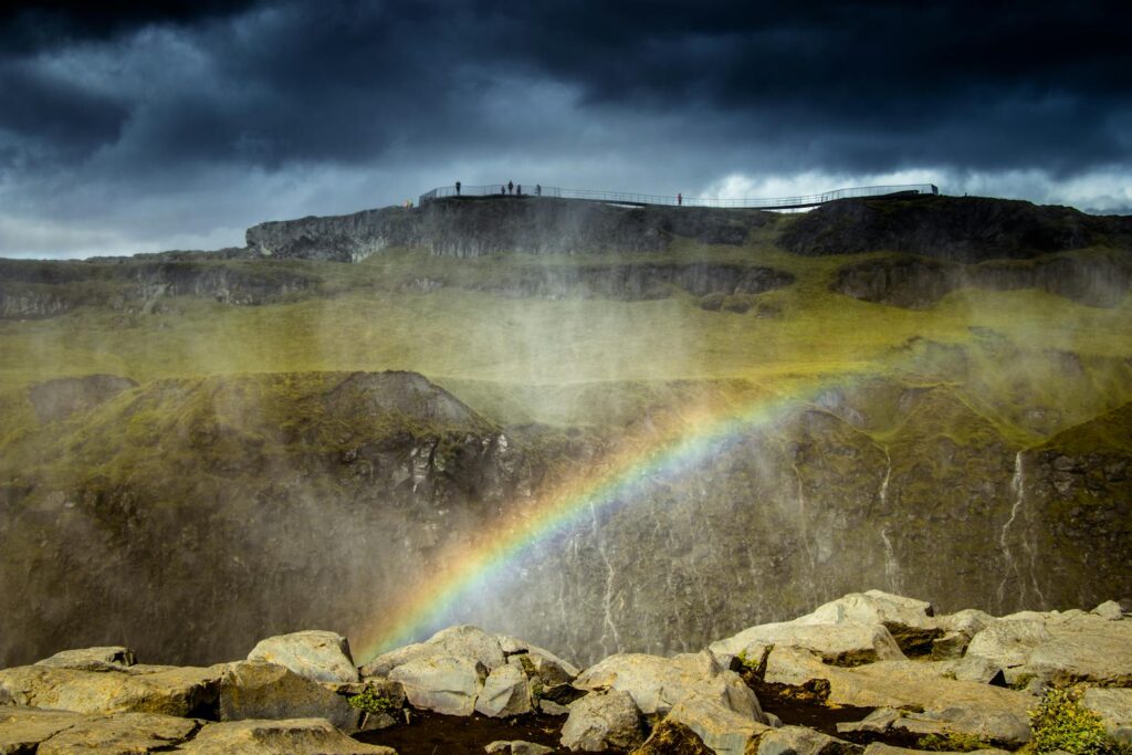 Scenic view of a rainbow over rocky Icelandic terrain with dark storm clouds.