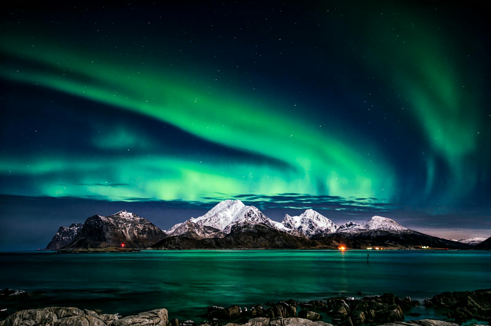 Breathtaking view of aurora borealis illuminating the snowy mountains of Lofoten Islands at night.