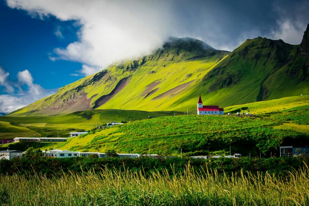 Beautiful landscape of a red-roofed church nestled in lush green hills under a vibrant sky in Iceland.